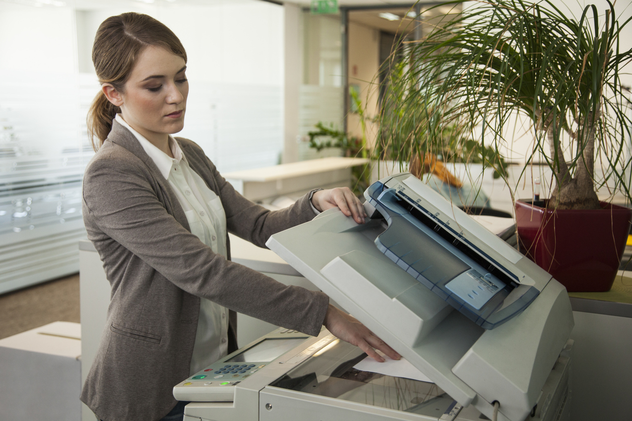 Young woman standing by photocopier/office printer in an office and making copies.